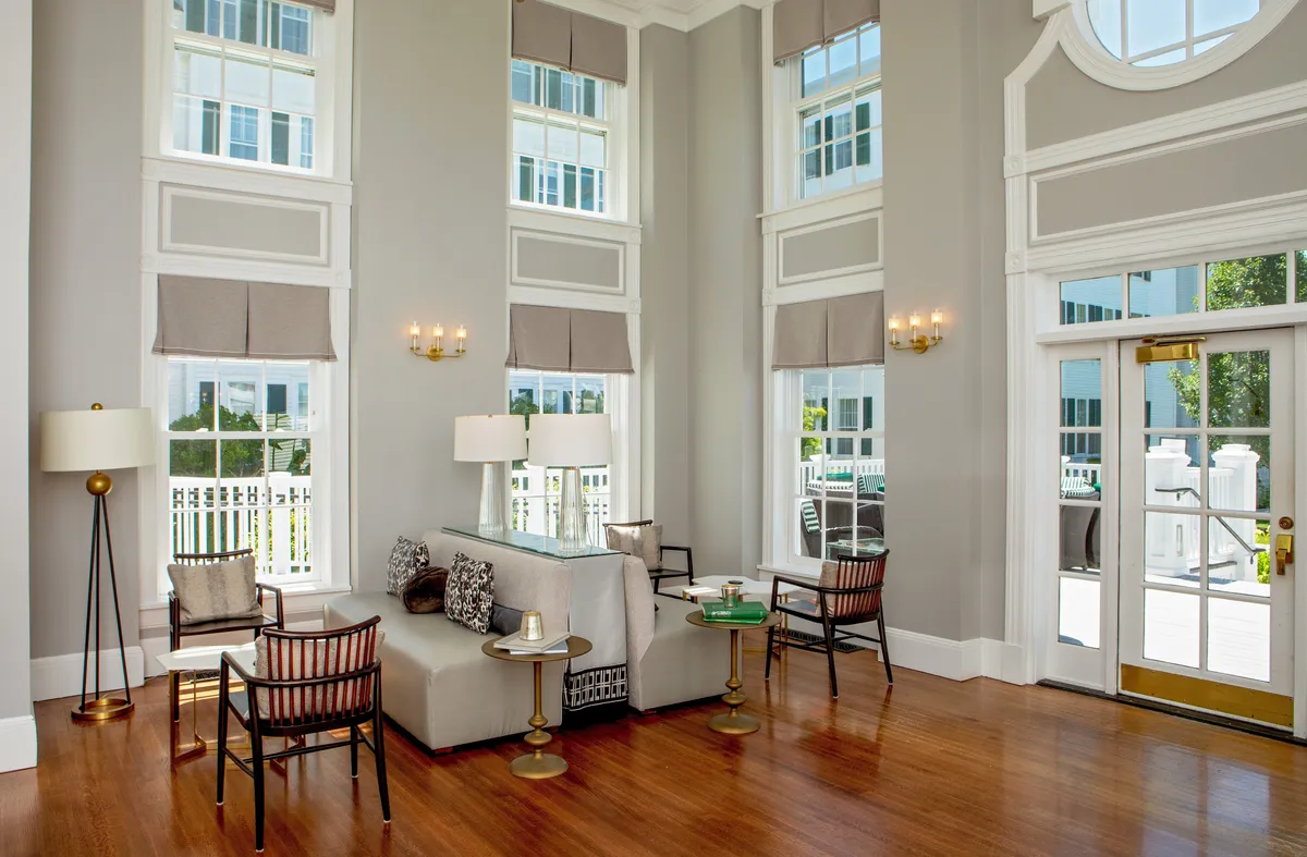 A bright, sophisticated seating area filled with natural light from large picture windows. Comfortable sofas and elegant décor create a welcoming setting for conversation or relaxation. The windows provide views of the outdoors, highlighting the connection to serene golf course vistas.