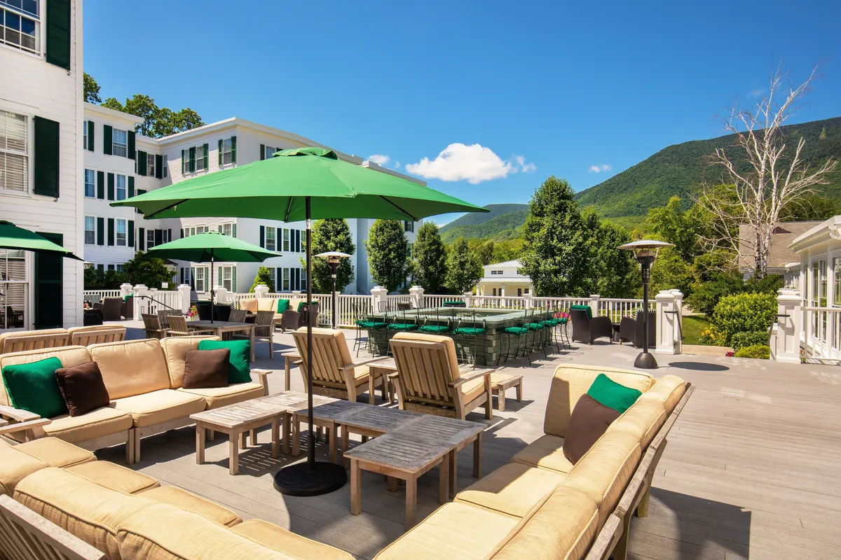 An inviting outdoor patio space with green umbrellas, comfortable seating, and a backdrop of beautiful mountain views. The space encourages outdoor socializing, dining, and enjoying the fresh air and natural beauty.
