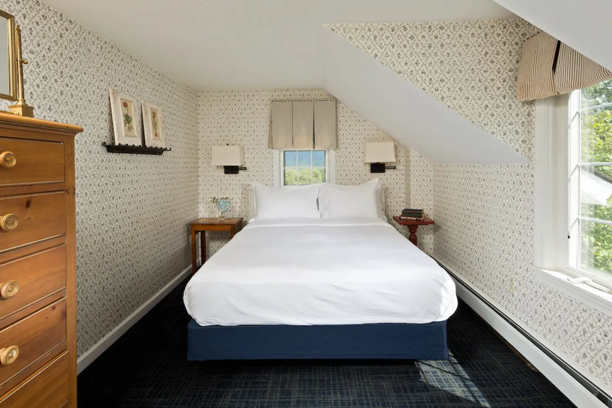 A sunlit bedroom with a plush bed, dresser, window views, and tasteful wall art. The setting is both elegant and comfortable, suggesting restful nights and serene mornings.
