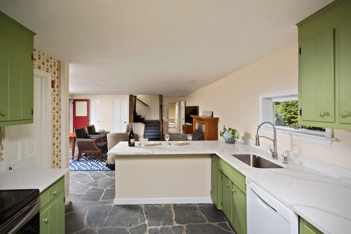 A close-up view of the kitchen's green cabinets, white countertop, stainless steel sink, and textured stone floor. The space feels open and functional, perfectly equipped for cooking together, prepping meals, and enjoying group activities in the kitchen.