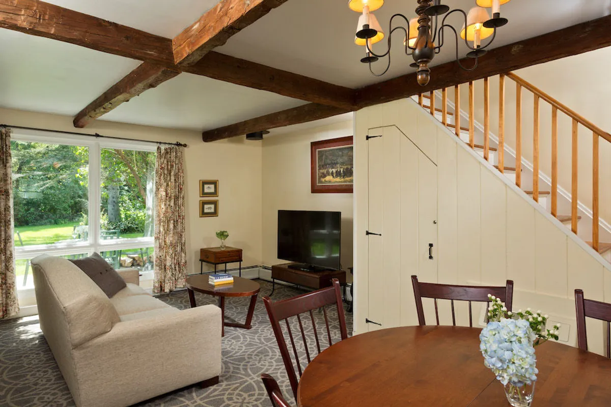 A spacious open-plan living and dining area featuring a plush sofa, a dining table, a stylish chandelier, and a staircase in the background. The layout is ideal for entertaining, game nights, or relaxed evenings, with multiple seating options for gatherings.