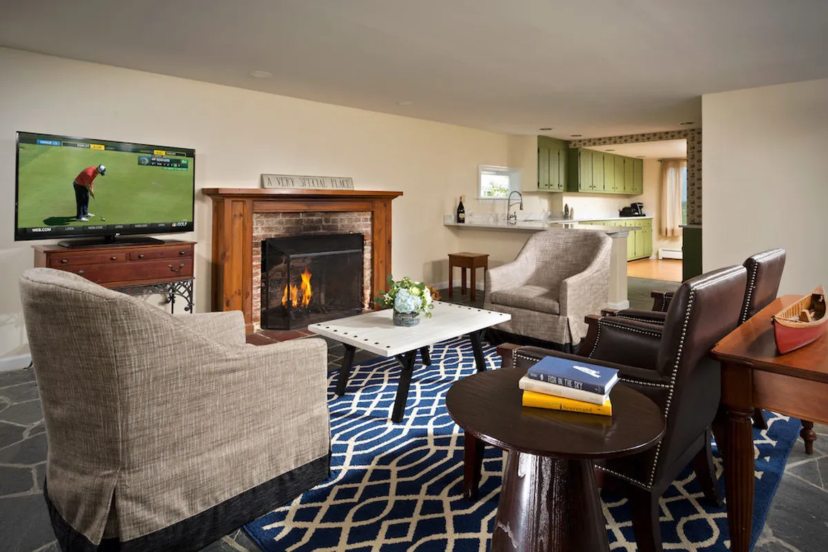 A cozy living room featuring a central fireplace, a plush rug, a comfortable sofa set, a coffee table, and a television. The room exudes warmth and invites both relaxation and social gatherings, making it ideal for movie nights or board games. Sunlight pours in, enhancing the space's inviting atmosphere.